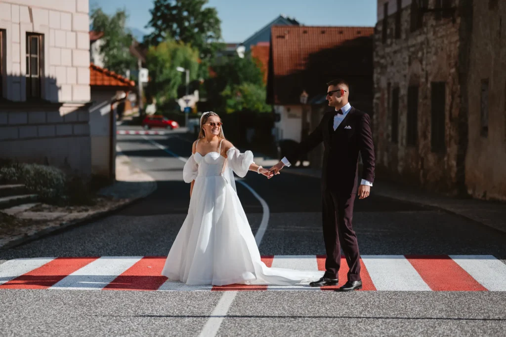 Nevesta a ženích sa držia za ruky na červeno-bielom prechode, téma ako si vybrať svadobného fotografa a cena služieb.